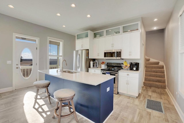 kitchen with sink, a kitchen island with sink, white cabinetry, stainless steel appliances, and a kitchen bar