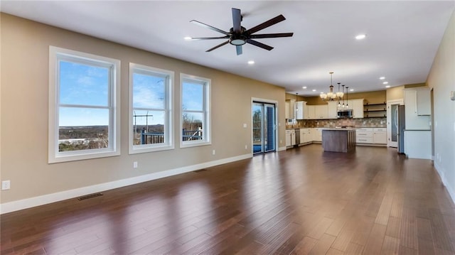 unfurnished living room featuring plenty of natural light, dark hardwood / wood-style flooring, and ceiling fan with notable chandelier