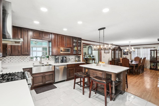 kitchen featuring pendant lighting, wall chimney range hood, sink, a breakfast bar, and appliances with stainless steel finishes