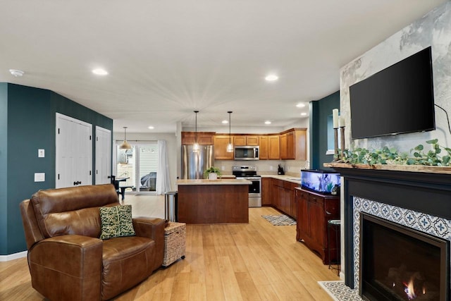 kitchen with a tile fireplace, a kitchen island, hanging light fixtures, stainless steel appliances, and light hardwood / wood-style flooring