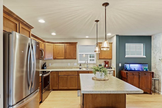 kitchen with sink, decorative light fixtures, a center island, appliances with stainless steel finishes, and light hardwood / wood-style floors