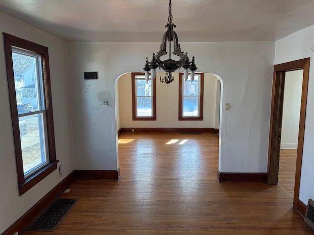 unfurnished dining area featuring wood-type flooring, a chandelier, and plenty of natural light