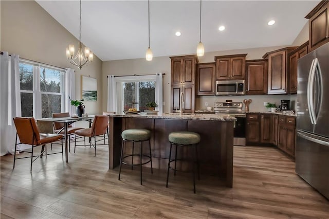 kitchen featuring decorative light fixtures, an island with sink, stainless steel appliances, light stone countertops, and hardwood / wood-style floors