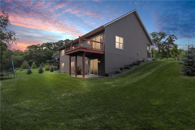 back house at dusk with a wooden deck, a yard, and a trampoline