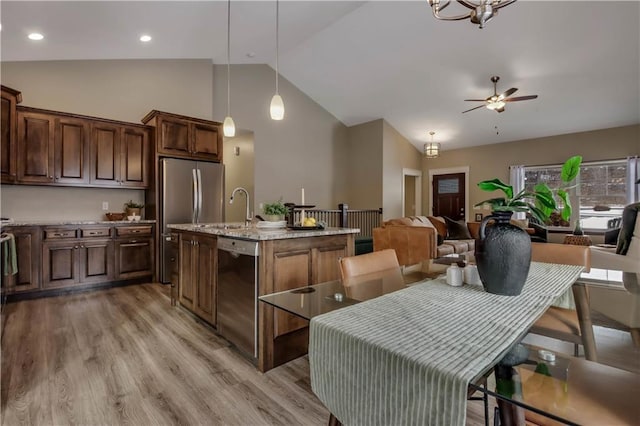 kitchen with lofted ceiling, light stone counters, appliances with stainless steel finishes, an island with sink, and pendant lighting