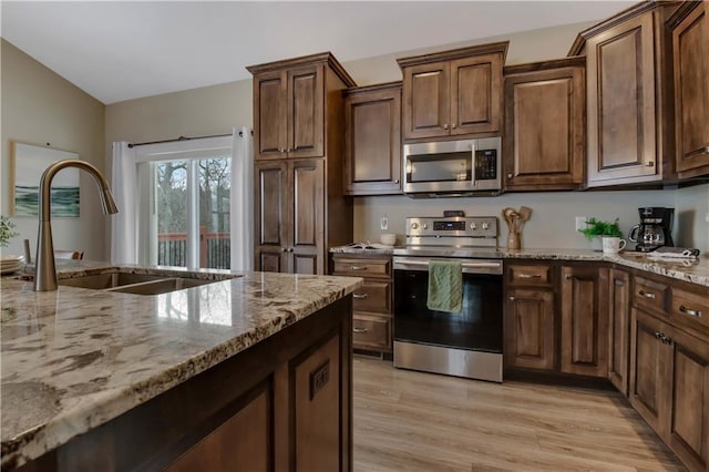 kitchen with vaulted ceiling, sink, light stone counters, stainless steel appliances, and light wood-type flooring