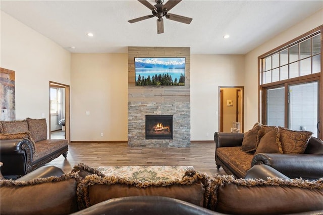 living room with ceiling fan, a stone fireplace, a high ceiling, and light wood-type flooring