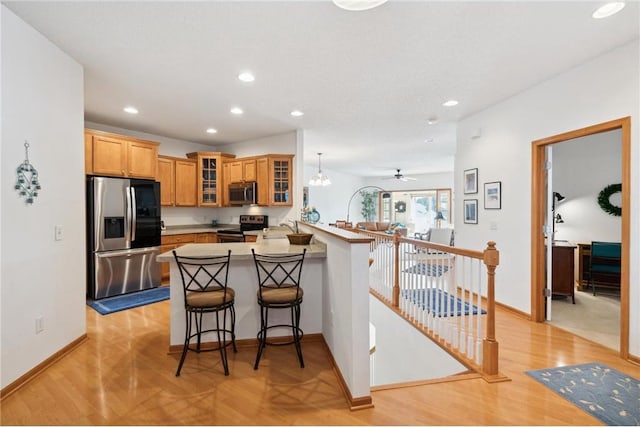 kitchen with stainless steel appliances, a breakfast bar, light hardwood / wood-style flooring, and kitchen peninsula