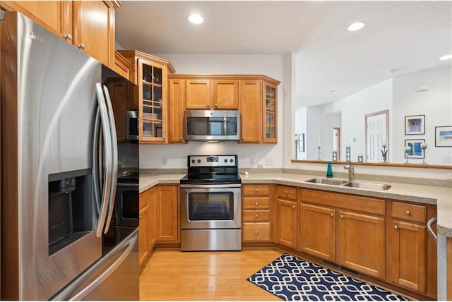 kitchen with sink, light wood-type flooring, stainless steel appliances, light stone countertops, and a textured ceiling