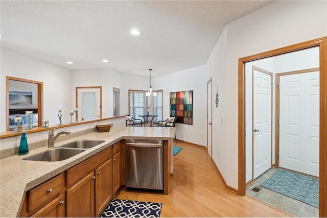 kitchen featuring sink, hanging light fixtures, a textured ceiling, stainless steel dishwasher, and kitchen peninsula