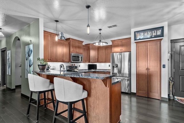 kitchen featuring pendant lighting, dark hardwood / wood-style flooring, stainless steel appliances, and dark stone countertops