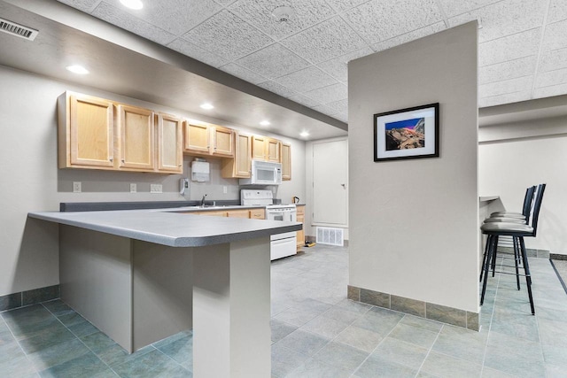 kitchen with white appliances, light brown cabinetry, a breakfast bar, and kitchen peninsula