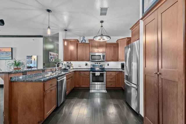 kitchen with sink, appliances with stainless steel finishes, hanging light fixtures, kitchen peninsula, and dark stone counters