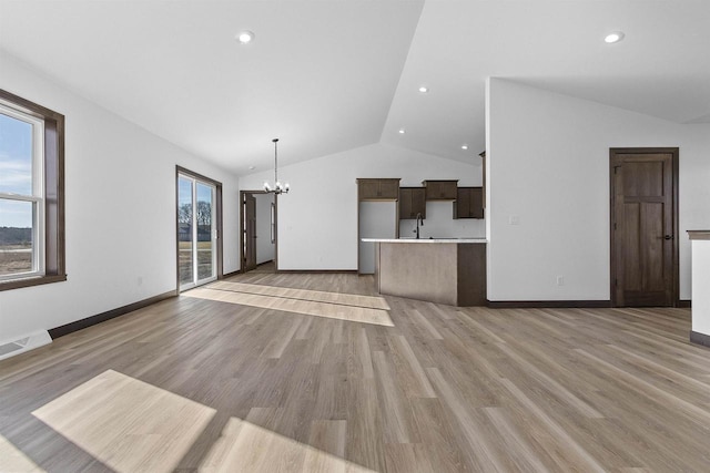 unfurnished living room with vaulted ceiling, a chandelier, and light wood-type flooring