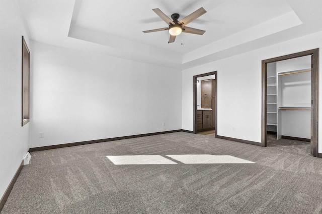 unfurnished bedroom featuring connected bathroom, a walk in closet, dark carpet, a tray ceiling, and a closet