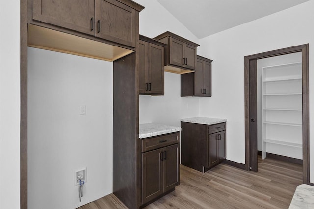 kitchen featuring light stone countertops, lofted ceiling, light wood-type flooring, and dark brown cabinetry