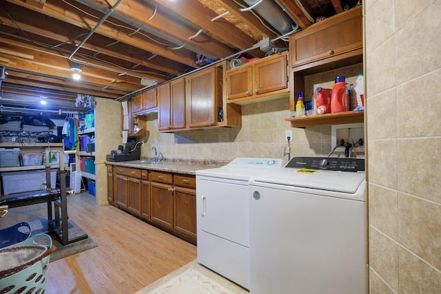 clothes washing area featuring sink, tile walls, cabinets, washing machine and clothes dryer, and light wood-type flooring