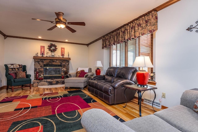 living room with hardwood / wood-style flooring, ceiling fan, a stone fireplace, and crown molding