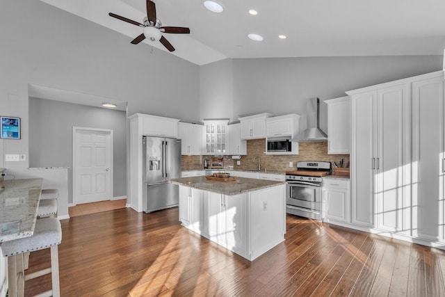 kitchen featuring stainless steel appliances, a kitchen breakfast bar, light stone countertops, white cabinets, and wall chimney exhaust hood