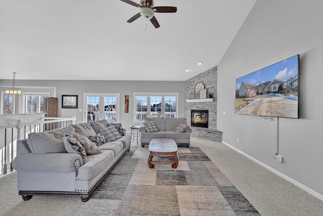 carpeted living room with ceiling fan, a stone fireplace, and high vaulted ceiling