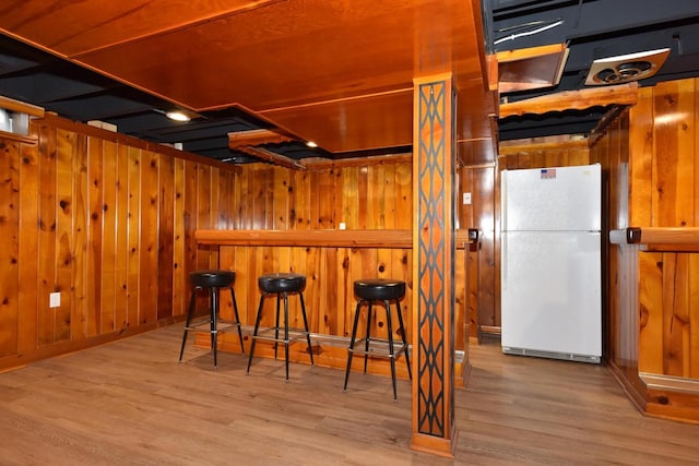 interior space featuring wood walls, a breakfast bar area, white fridge, and light hardwood / wood-style flooring