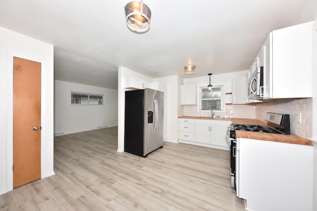 kitchen featuring sink, hanging light fixtures, stainless steel appliances, white cabinets, and wood counters