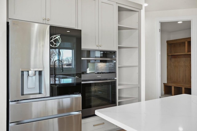 kitchen featuring stainless steel refrigerator, light stone countertops, double oven, and white cabinets