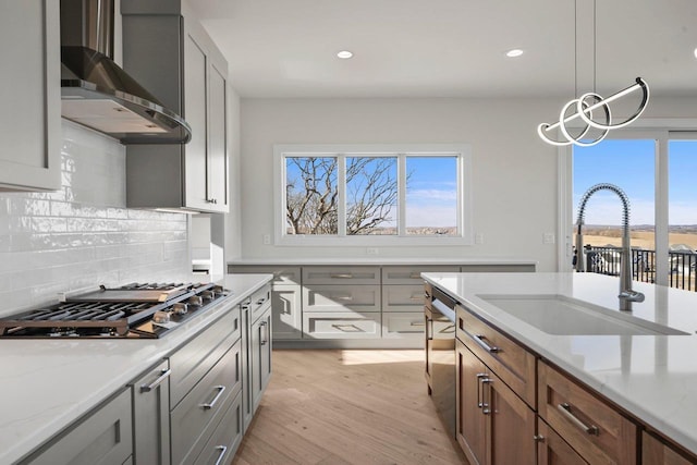 kitchen with wall chimney exhaust hood, sink, light stone counters, hanging light fixtures, and appliances with stainless steel finishes