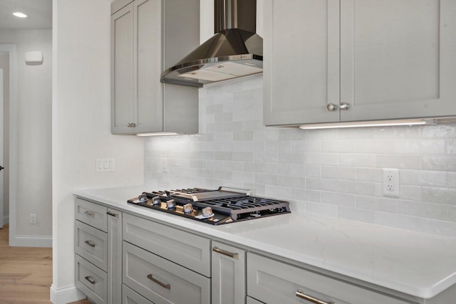 kitchen with wall chimney exhaust hood, gray cabinetry, light hardwood / wood-style flooring, stainless steel gas stovetop, and decorative backsplash