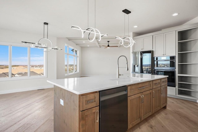 kitchen with sink, dishwasher, double oven, white cabinets, and a center island with sink