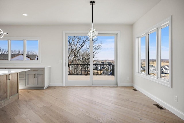 unfurnished dining area with an inviting chandelier and light wood-type flooring