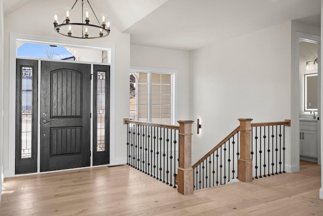 foyer entrance with vaulted ceiling, a chandelier, sink, and light wood-type flooring