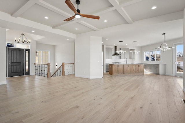 unfurnished living room with sink, light hardwood / wood-style flooring, coffered ceiling, ceiling fan with notable chandelier, and beamed ceiling