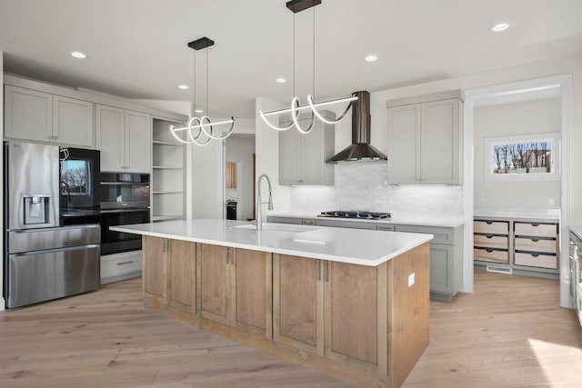 kitchen featuring pendant lighting, stainless steel appliances, a kitchen island with sink, and wall chimney range hood