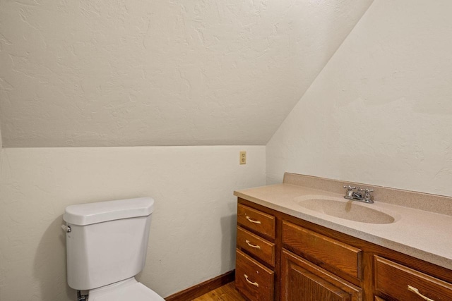 bathroom featuring vaulted ceiling, wood-type flooring, vanity, toilet, and a textured ceiling