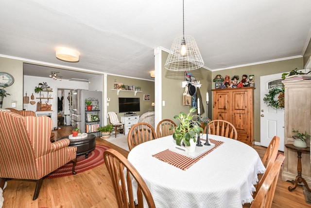 dining space with ornamental molding and light hardwood / wood-style flooring