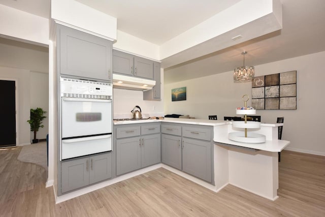 kitchen featuring pendant lighting, gray cabinets, oven, and light hardwood / wood-style flooring