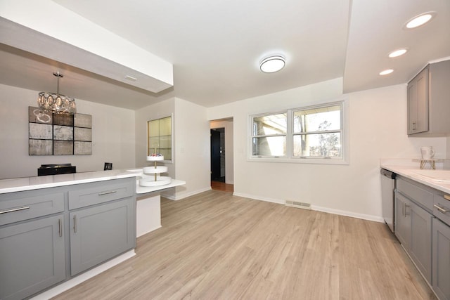 kitchen with gray cabinetry, pendant lighting, stainless steel dishwasher, and light wood-type flooring