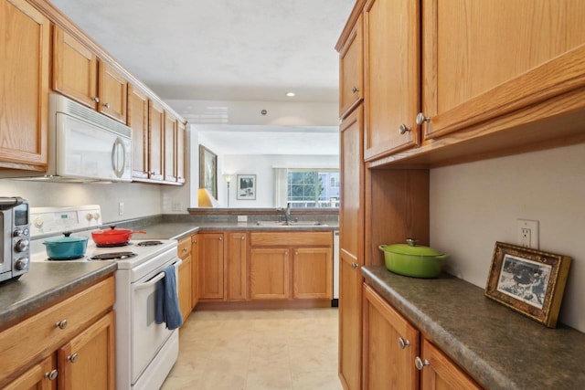 kitchen featuring white appliances, brown cabinetry, dark countertops, and a sink