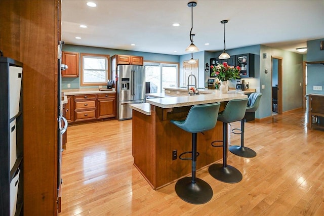 kitchen featuring high end fridge, a kitchen island with sink, light hardwood / wood-style floors, and decorative light fixtures