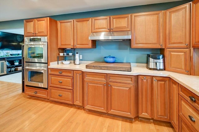 kitchen with black electric stovetop, stainless steel double oven, and light hardwood / wood-style flooring