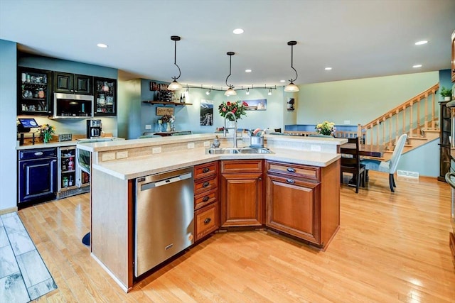 kitchen with sink, hanging light fixtures, light hardwood / wood-style flooring, appliances with stainless steel finishes, and a kitchen island with sink