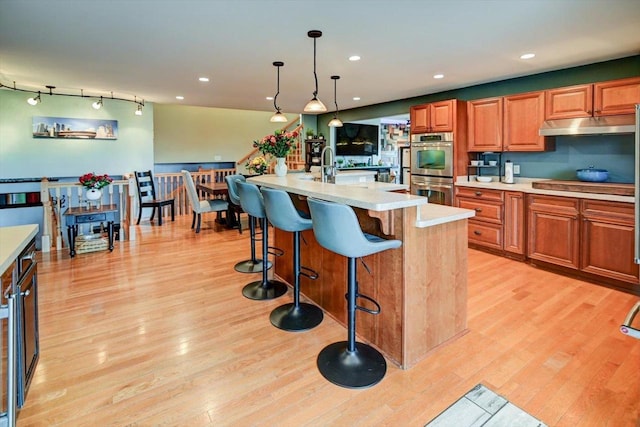 kitchen featuring an island with sink, pendant lighting, stainless steel double oven, and light hardwood / wood-style floors