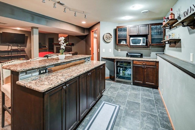 kitchen featuring a kitchen island, stainless steel microwave, a breakfast bar area, beverage cooler, and dark brown cabinets