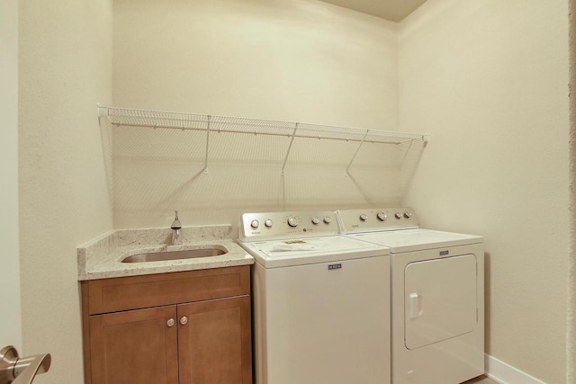 clothes washing area featuring cabinets, sink, and washer and clothes dryer