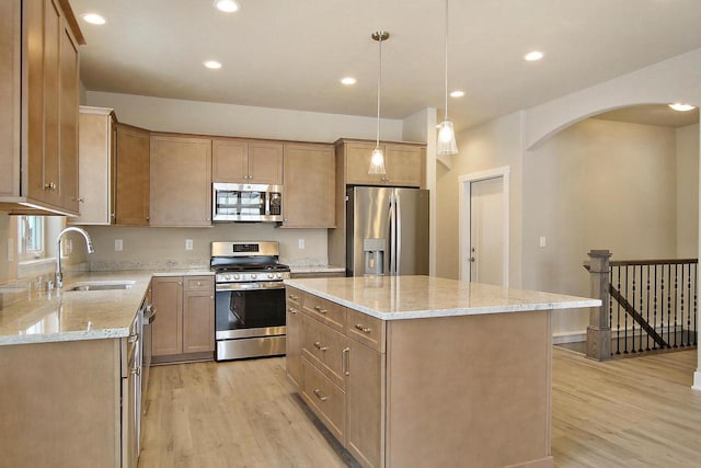 kitchen with appliances with stainless steel finishes, sink, hanging light fixtures, a center island, and light hardwood / wood-style flooring