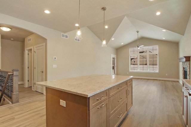 kitchen featuring vaulted ceiling, a stone fireplace, decorative light fixtures, a center island, and light wood-type flooring