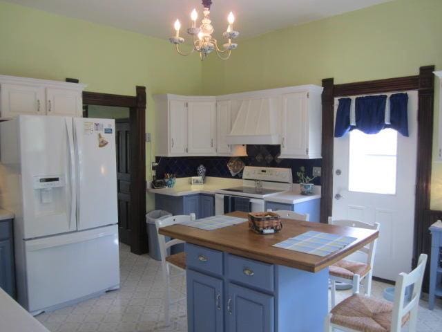 kitchen featuring premium range hood, blue cabinetry, white cabinetry, pendant lighting, and white appliances