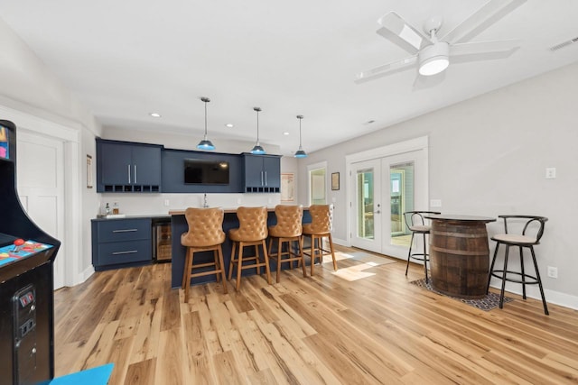 kitchen featuring french doors, blue cabinets, hanging light fixtures, light hardwood / wood-style flooring, and a kitchen breakfast bar