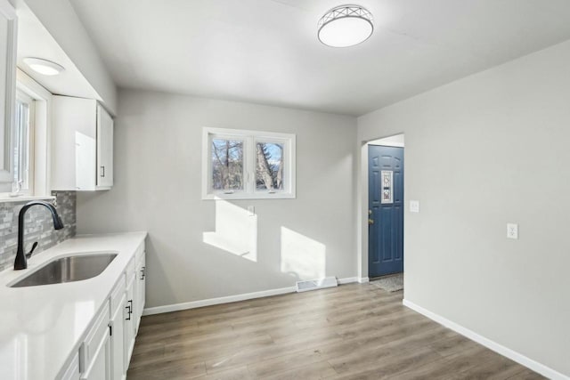 kitchen featuring tasteful backsplash, white cabinetry, sink, and light hardwood / wood-style flooring